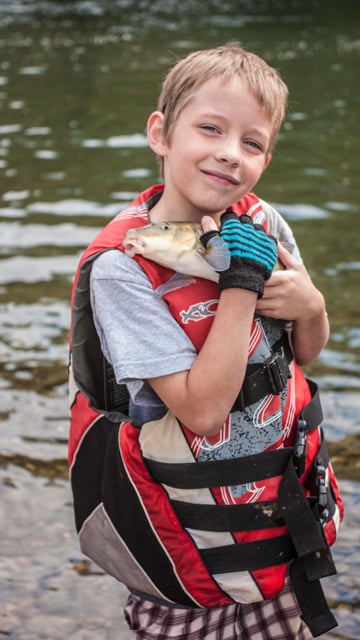 smiling boy holding close a fish he caught