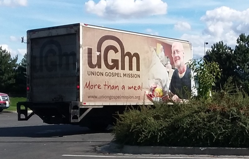 Paul is on the side of the truck Larry drives to pick up donations from UGM's food partners.